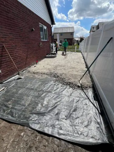 Professional Sportzturf crew members installing heavy-duty black geotextile weed barrier fabric and spreading base material in a residential side yard.