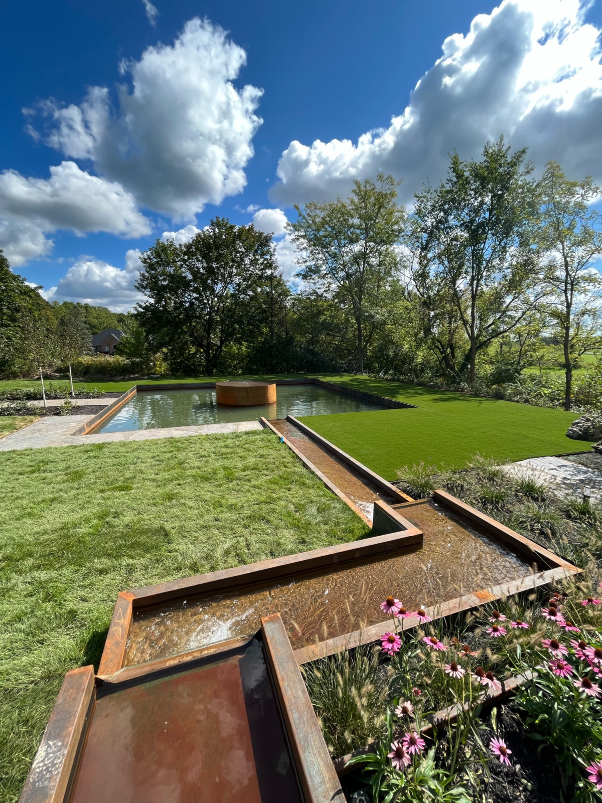 Modern backyard landscaping in Michigan featuring Sportzturf artificial grass and custom water features.