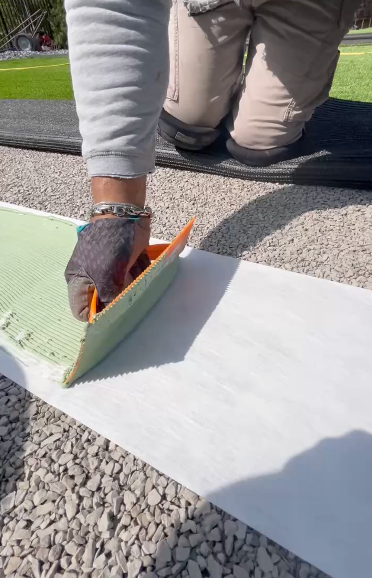 A close-up of a professional artificial turf installation showing a technician applying specialized green adhesive onto industrial seam tape between two sections of synthetic grass.
